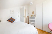 a white bedroom with a bed and a pink chair