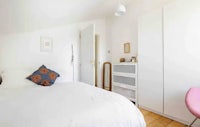 a white bedroom with a bed and a pink chair