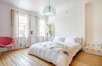 a white bedroom with wooden floors and a pink chair