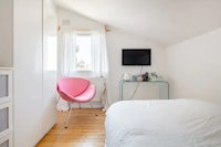 a white bedroom with a pink chair and a tv